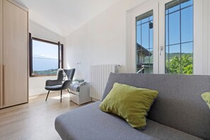 Una stanza moderna con un divano grigio, un cuscino verde, un armadio in legno, una sedia e una scrivania con vista sull'esterno.