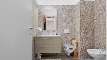 Une salle de bain moderne avec un mur carrelé, un lavabo, des toilettes et un bidet.