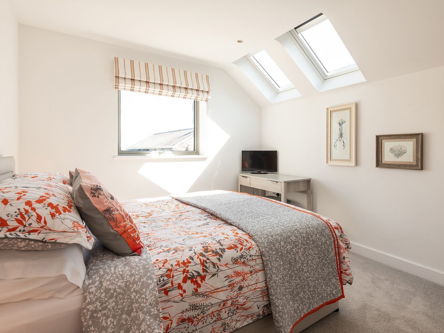 A bedroom with a bed, a TV, a desk, and two skylights.