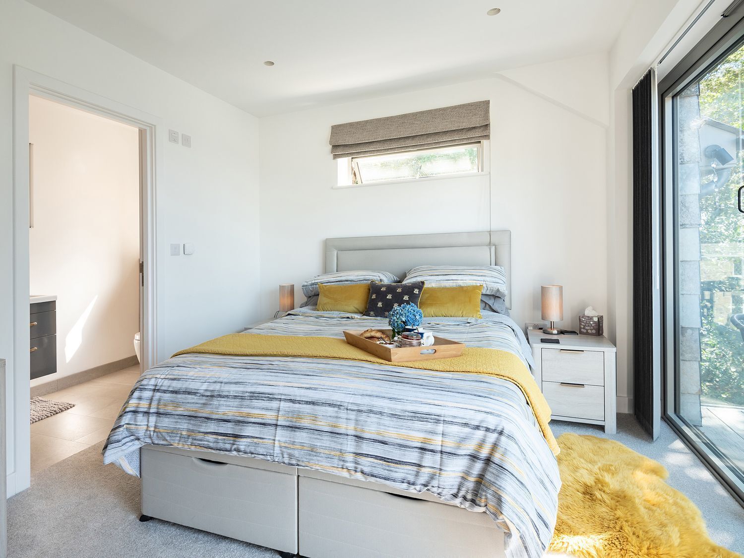 A modern bedroom with a large bed, bedside tables, a window with a view, and a door leading to another room.