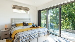 Un dormitorio con cama, mesita de noche, lámpara y vistas al exterior a través de un ventanal amplio.