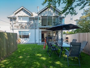 A modern two-story house with a patio area featuring a table and chairs, a large umbrella, and a wooden fence.