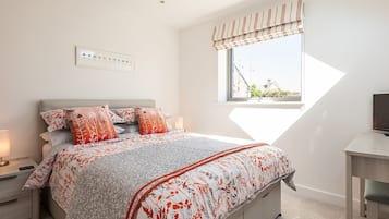 A bedroom with a bed, bedside tables, a window with curtains, and a view of buildings outside.