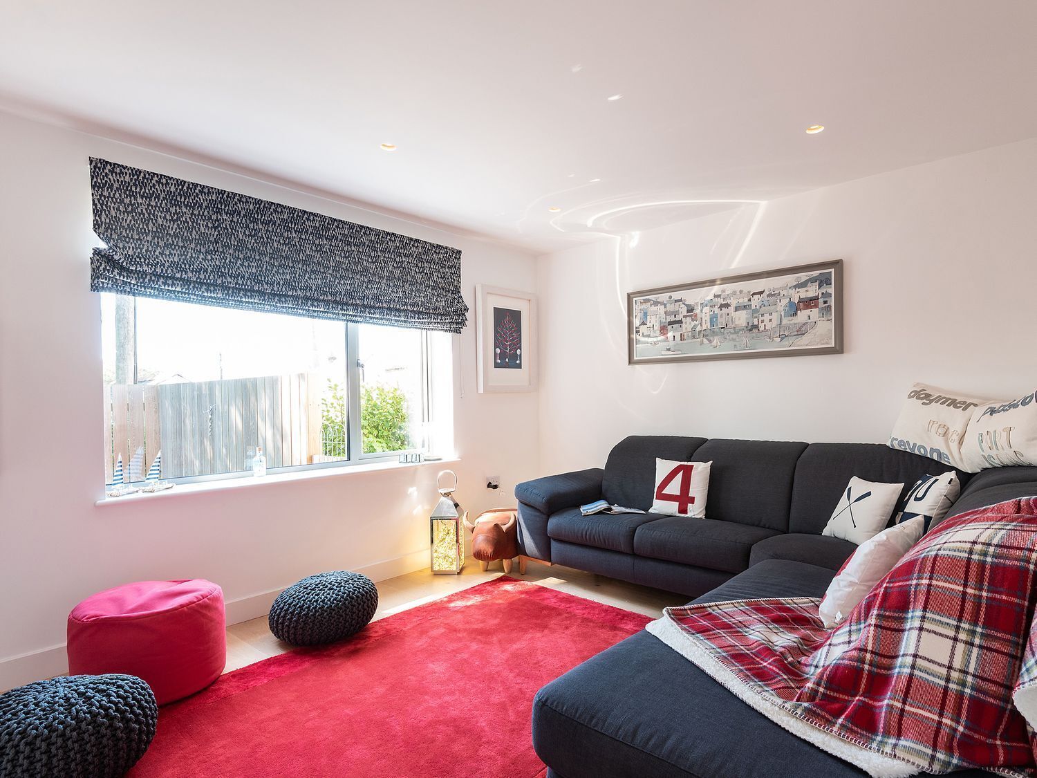 Een woonkamer met een bank, poefs, een rood vloerkleed en een raam met uitzicht.