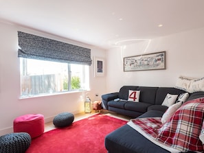 A living room with a sofa, ottomans, a red rug, and a window with a view. - Pentire (Wadebridge)