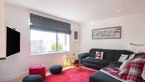 Una sala moderna con un sofá gris, un reposapiés rojo y una alfombra roja.