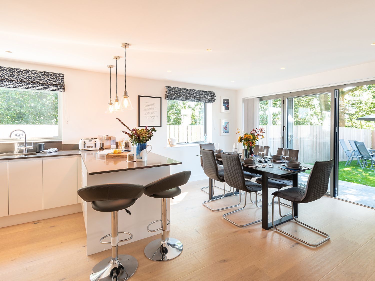 Een moderne keuken met een centraal eiland, barstoelen en een eethoek met een tafel en stoelen.