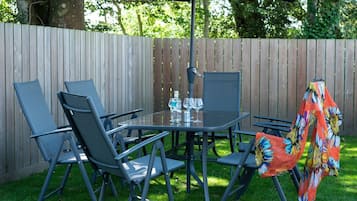 A patio with a glass table, four chairs, a large umbrella, and a wooden fence.