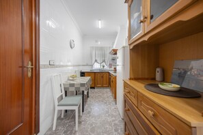 Une cuisine de taille réduite comprenant une table à manger, des chaises, un réfrigérateur et des armoires en bois.