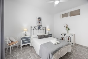 Een slaapkamer met een bed, nachtkastjes, een stoel, een dressoir en een plafondventilator.