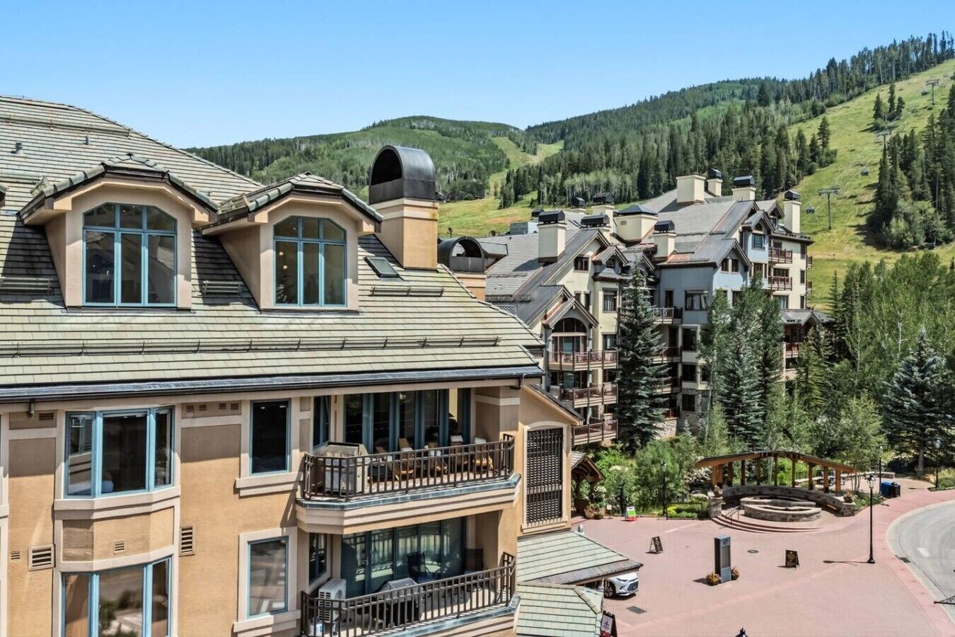 A multi-story hotel with balconies, a ski lift in the background, and a mountainous landscape.