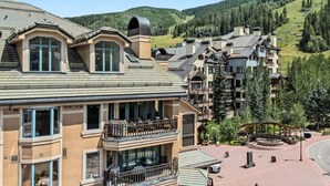 A multi-story hotel with balconies, a ski lift in the background, and a mountainous landscape. - Village Luxe | Ski-in/Ski-out | Heated Pool & Spa (Beaver Creek)