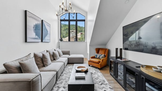A modern living room with a large window, a sofa, a coffee table, a leather armchair, and a flat-screen TV. - Village Luxe | Ski-in/Ski-out | Heated Pool & Spa (Beaver Creek)