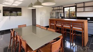 A modern kitchen with a dining area, featuring a large table, wooden chairs, pendant lighting, and a view of the outdoors. - LK Santa Efigênia 2 (Belo Horizonte)