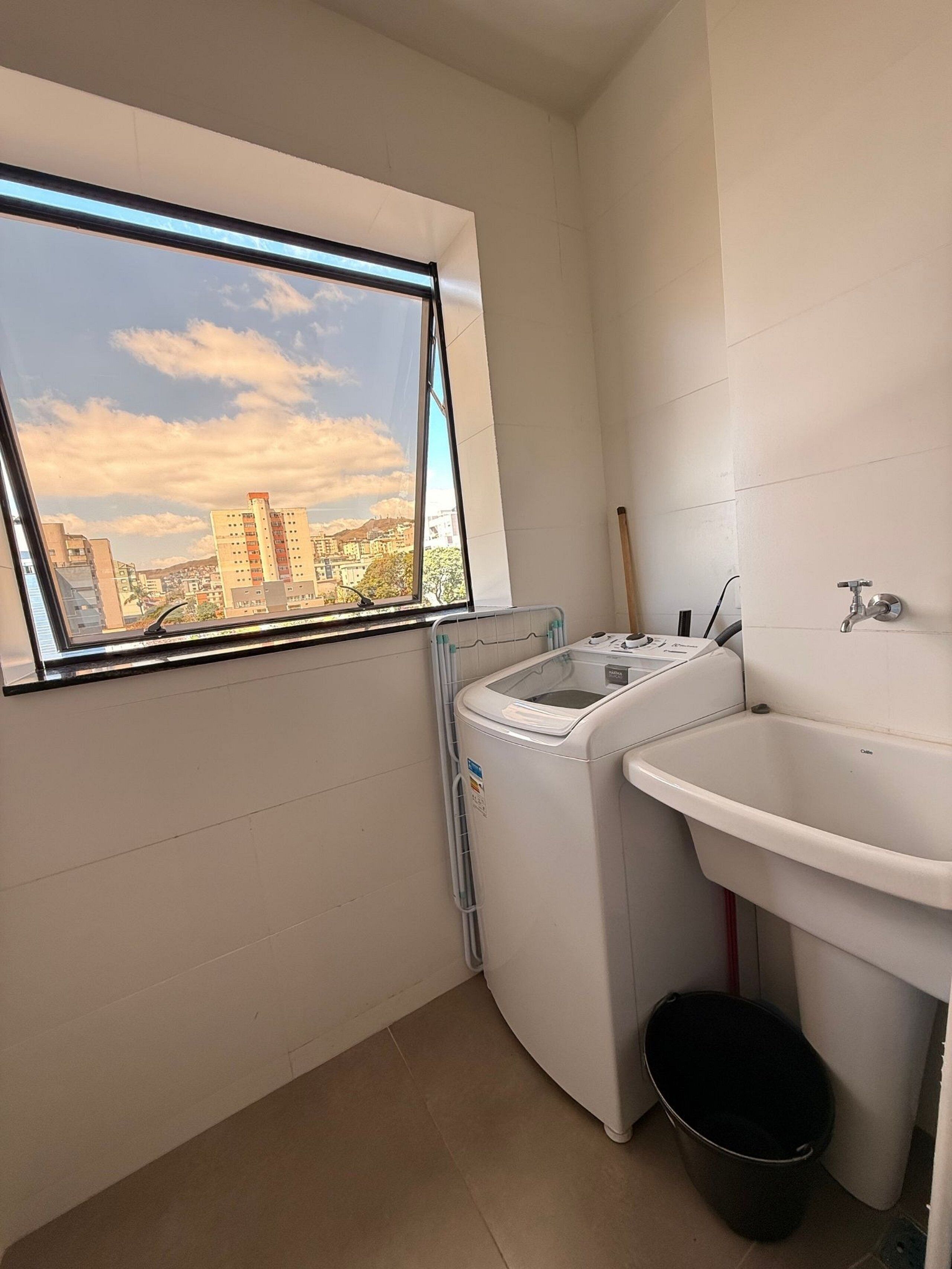 A small laundry room with a washing machine, a sink, and a window with a city view.