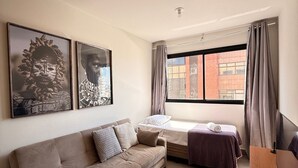 A modern hotel room with a sofa, a bed, a TV, and artwork on the wall. - LK Santa Efigênia 2 (Belo Horizonte)
