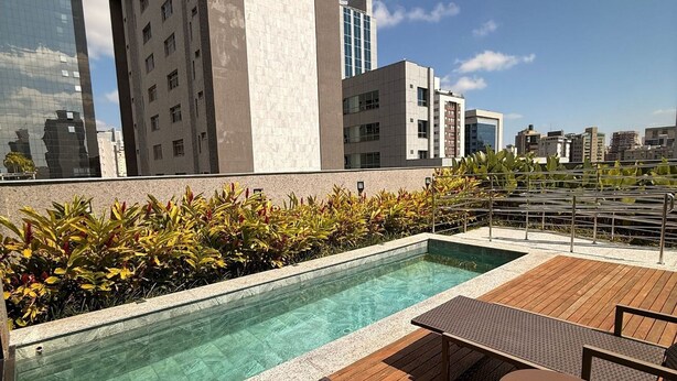 A rooftop pool with wooden deck and lounge chairs, surrounded by buildings. - LK Santa Efigênia 2 (Belo Horizonte)