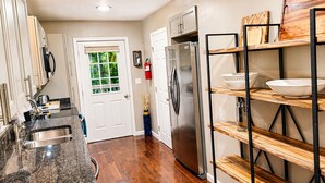 Una cocina con refrigerador de acero inoxidable, estantes de madera y una ventana que ofrece vistas al verdor.