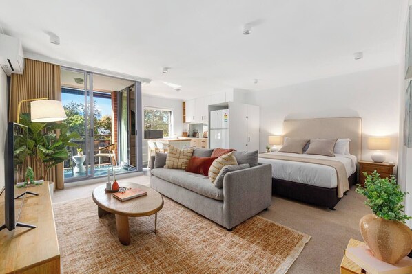 A modern hotel room with a sofa, a bed, a dining area, and a balcony with a view. - The Surry Studio Cosy Stay near Cafs and Nightlife (Surry Hills)