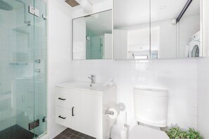 A modern bathroom with a glass shower enclosure, a white sink with a mirror above, and a toilet. - The Surry Studio Cosy Stay near Cafs and Nightlife (Surry Hills)
