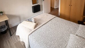 Ein Schlafzimmer mit Bett, Nachttisch, Spiegel, Kleiderschrank und einer Tür zu einem anderen Raum.
