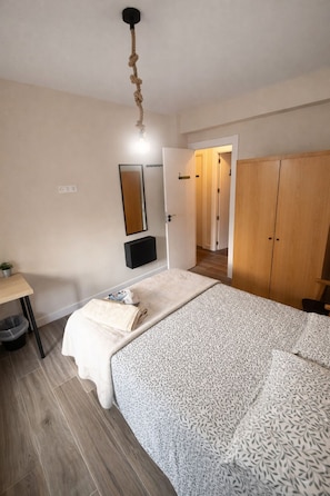 A bedroom with a bed, a bedside table, a mirror, a wardrobe, and a door leading to another room.
