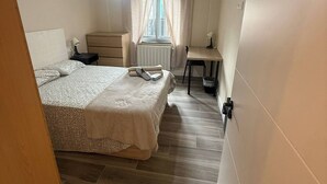 Ein Schlafzimmer mit Bett, Schreibtisch, Stuhl, Heizkörper und einem Fenster mit Vorhängen.