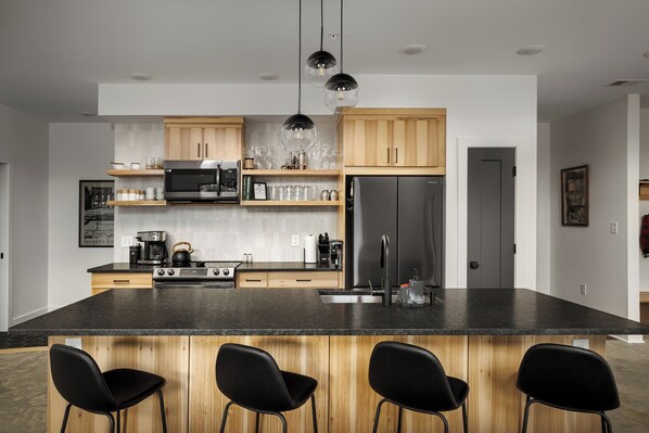 A modern kitchen with a central island, wooden cabinets, a stainless steel refrigerator, and black bar stools. - Modern Cabin, Kids' Playhouse, Firepit, 5acres, across river from Harpers Ferry (Knoxville)