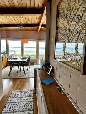 A modern interior with a wooden ceiling, a dining area with a view of the sea, and a decorative leaf pattern on the wall. - Enjoy Camano Tidalwilds waterfront beach house w/ hot tub, sups, kayak and more! (Camano)