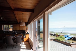 A modern kitchen with a dining area, large windows, and a view of the water. - Enjoy Camano Tidalwilds waterfront beach house w/ hot tub, sups, kayak and more! (Camano)