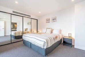 Ein modernes Schlafzimmer mit einem großen Bett, einem Nachttisch, einem Spiegel und Kunstwerken an der Wand.