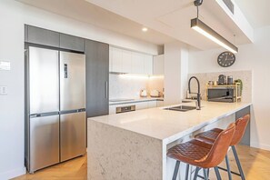 Eine moderne Küche mit einem Edelstahl-Kühlschrank, einer Marmorarbeitsplatte, einem Spülbecken und zwei Ledersitzhocker.