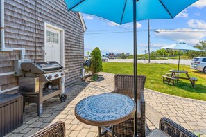 An outdoor patio with a grill, wicker furniture, and a table under a blue umbrella.