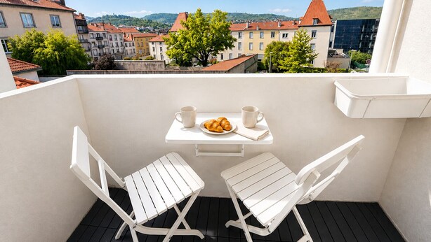 A balcony with two white chairs, a small table, and a plate of croissants.