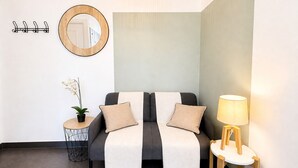 A modern room with a grey sofa, a small round table with a lamp, a mirror, and a wall-mounted coat rack.