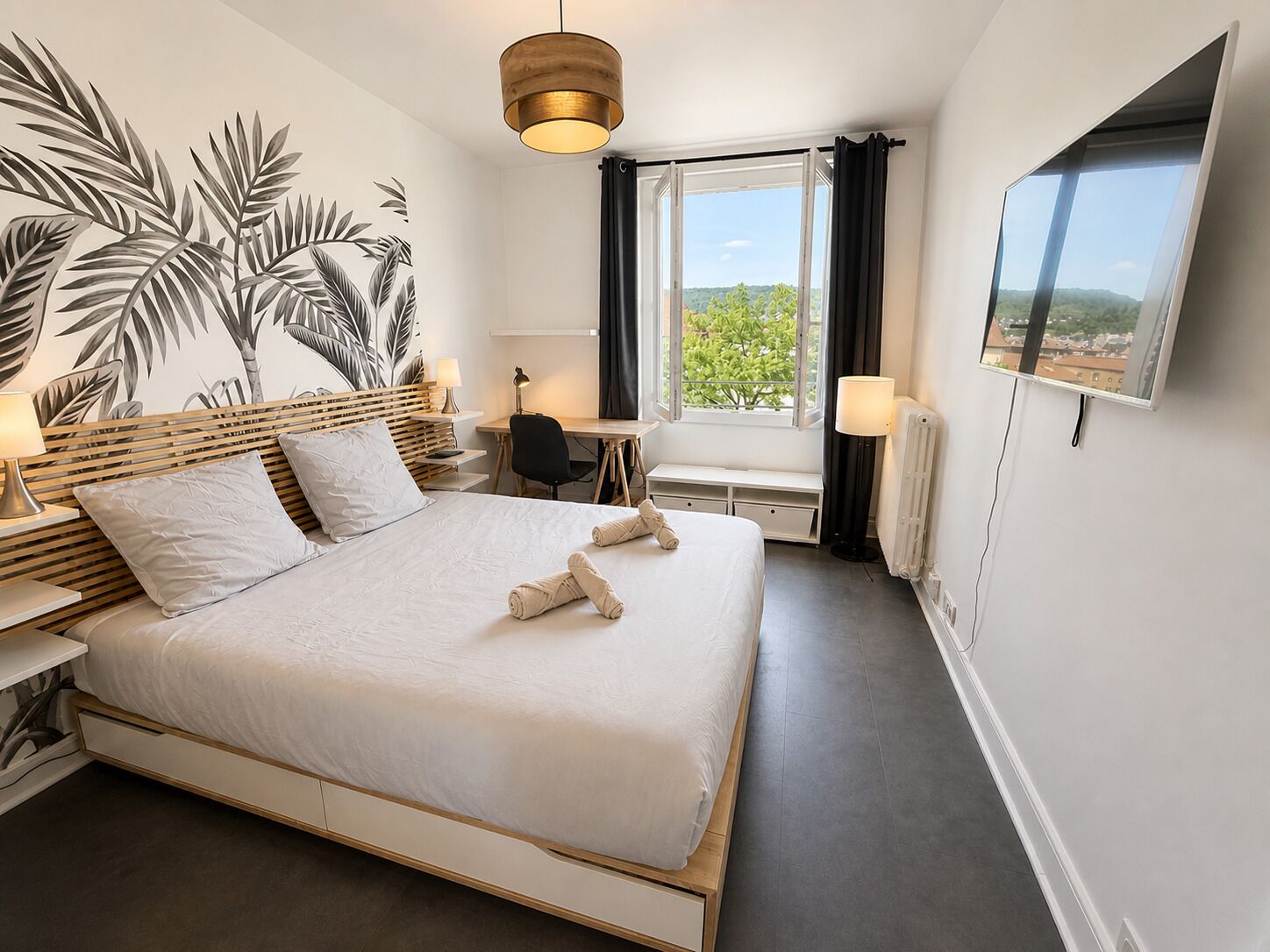 A hotel room with a bed, a desk, a chair, a TV, and a window with a view.