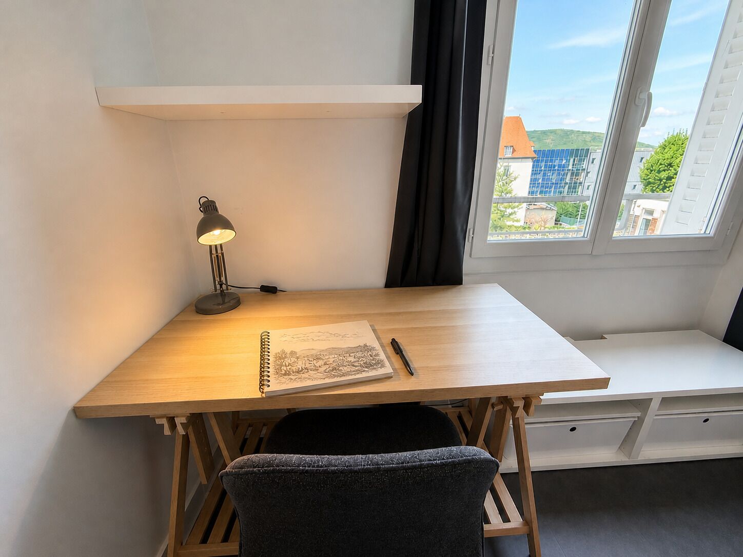 Ein Arbeitsplatz mit Schreibtisch, Stuhl, Lampe und Notizbuch.