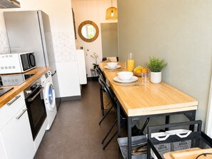 Een kleine keuken met een houten tafel, een wasmachine, een magnetron en een spoelbak.