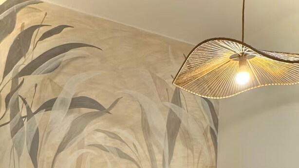 A bedroom with a bed, wooden headboard, and a wall with a leaf pattern.