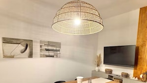 A dining area with a wooden table, black chairs, a woven pendant light, and artwork on the walls.