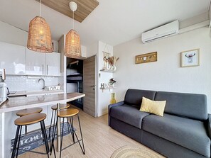 Eine moderne Küche mit einer zentralen Kochinsel, Barhocker, einem dunkelgrauen Sofa mit Kissen und einer Pendelleuchte.