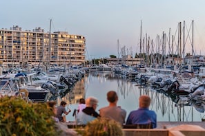 Ein Yachthafen mit vertäuten Booten, ein Gebäude mit Balkonen und Personen, die auf einem Deck sitzen.