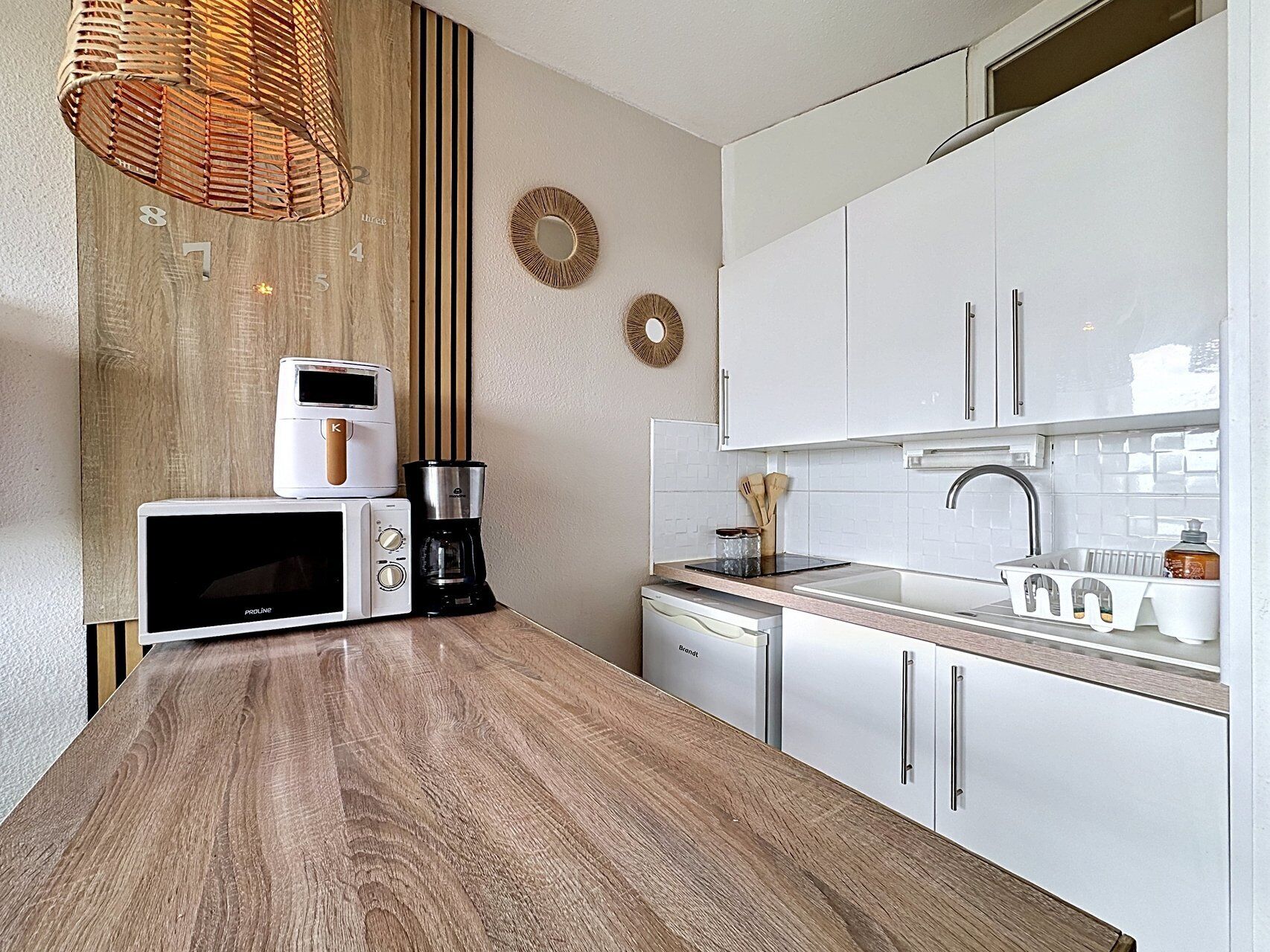 Une cuisine moderne avec des armoires blanches, un plan de travail en bois, un four à micro-ondes, une machine à café et un luminaire suspendu.