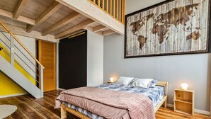 Een slaapkamer met een houten bed, een wereldkaart aan de muur, een trap en een klein nachtkastje met een lamp.