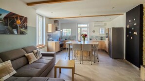 Een moderne keuken met een centraal eiland, een eethoek met tafel en stoelen, een bank en een koelkast.