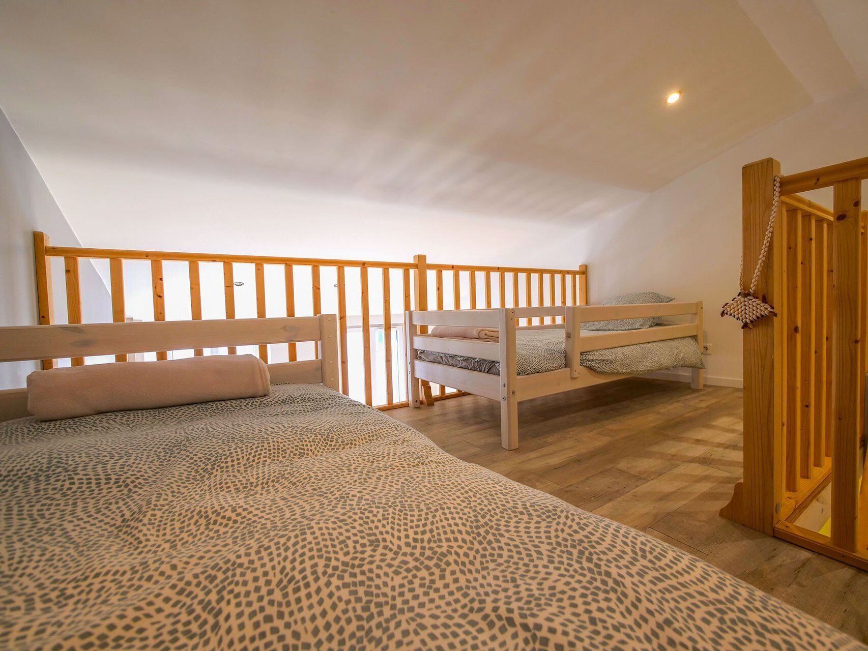 A loft bedroom with a sloped ceiling, wooden railings, and a bed with a patterned bedspread.