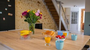 Een ontbijttafel met fruit, bloemen en sap in een kamer met een stenen muur en een trap.