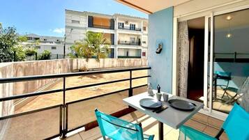 En balkon med et bord og stole, udsigt til bygninger og en dør, der fører til et indre rum.
