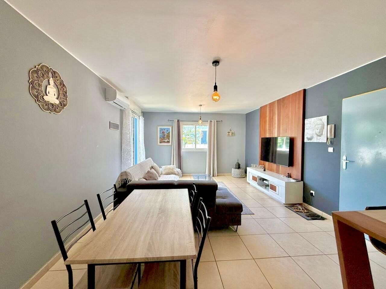 A modern living room with a dining table, sofa, TV, and decorative wall piece.