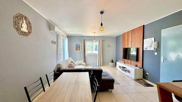 A modern living room with a dining table, sofa, TV, and decorative wall piece.
